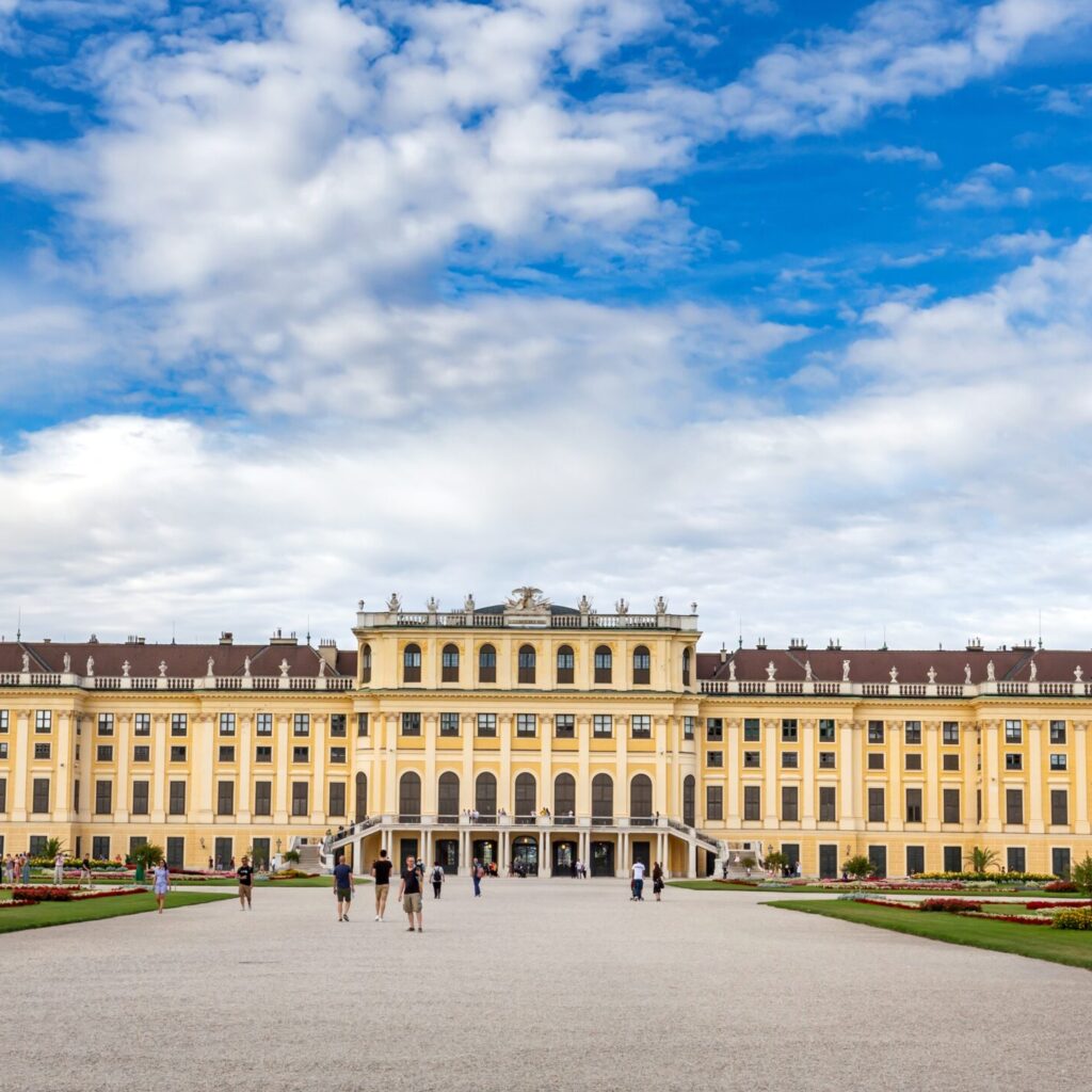 A wide-angle shot of schönbrunn palace in vienna, austria with a cloudy blue sky in the background